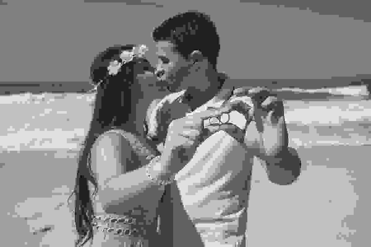 casal de noivos se beijam segurando as alianças em praia no rio de janeiro