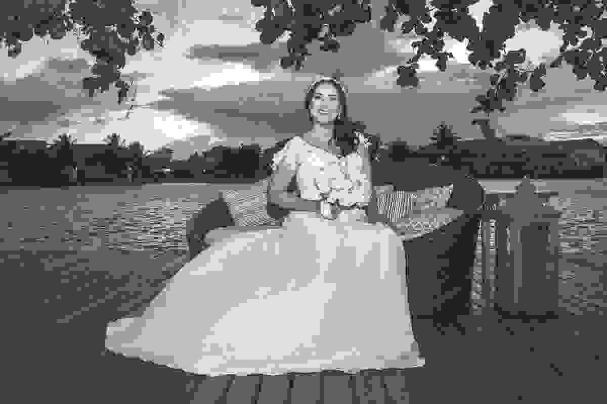 Fotografia da noiva após a cerimonia possando para foto sentada em um puff com o canal de Cabo Frio ao fundo