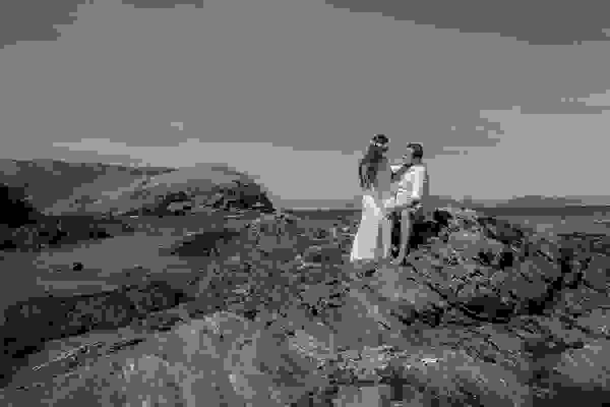 Casal sentado em pedras com o mar ao fundo em lindo cenário da praia do forte em cabo frio rio de janeiro