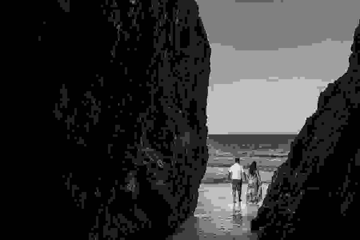Fotografia mostra casal caminhando de costas saindo da gruta do amor em arraial do cabo em ensaio pré casamento