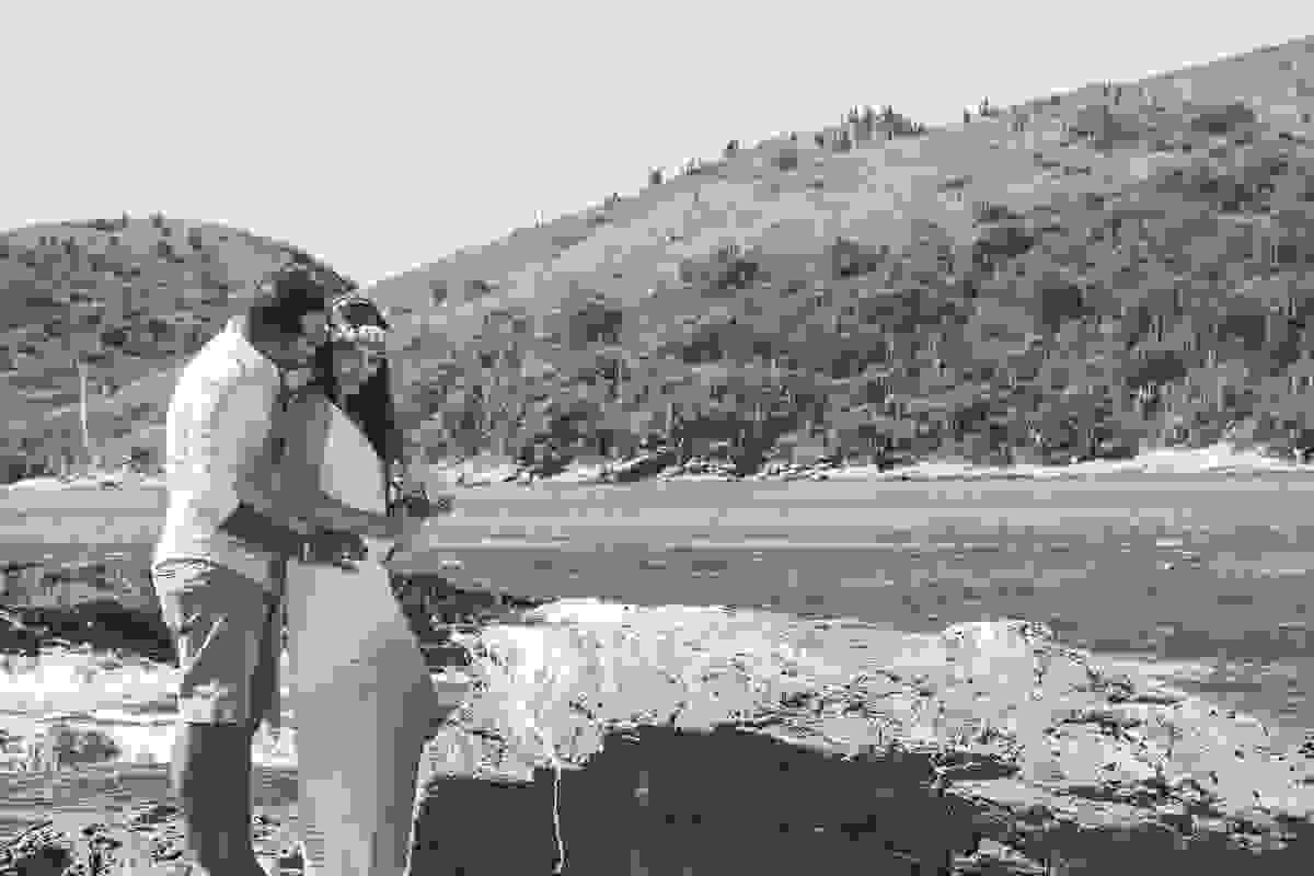 fotografia de ensaio pré casamento em cabo frio rio de janeiro mostra casal de pé noiva segurando bouquet enquanto noivo a abraça.