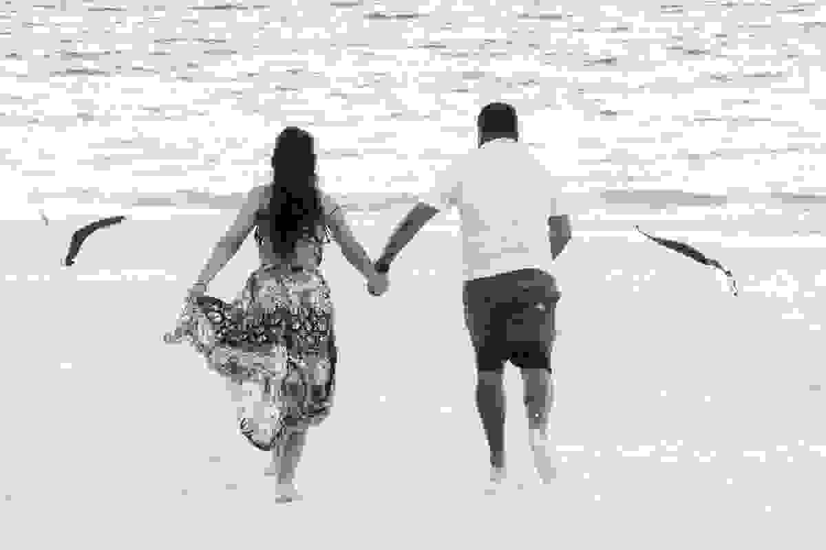 Book pré casamento em arraial do cabo mostra casal de costas correndo pela areia da praia enguanto garças voam ao lado
