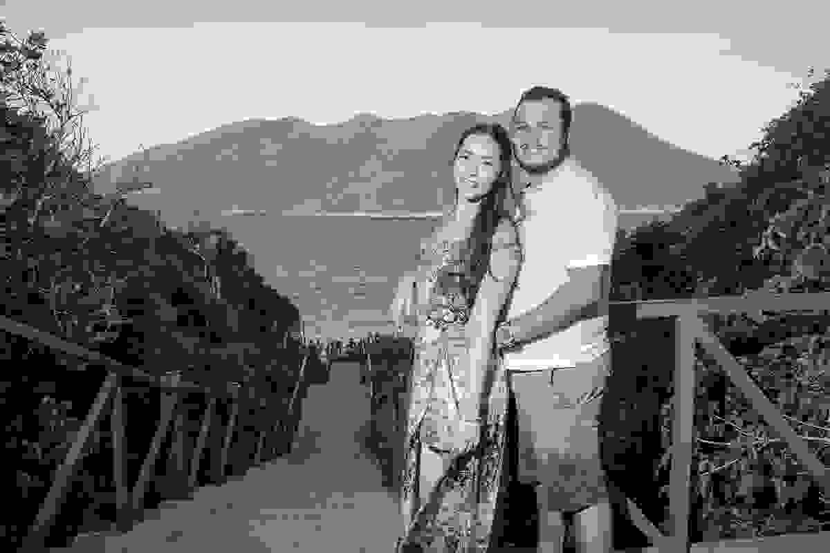 Fotografia mostra casal posando de frente para a escadaria que dá acesso as praias do atalaia em arraial do cabo