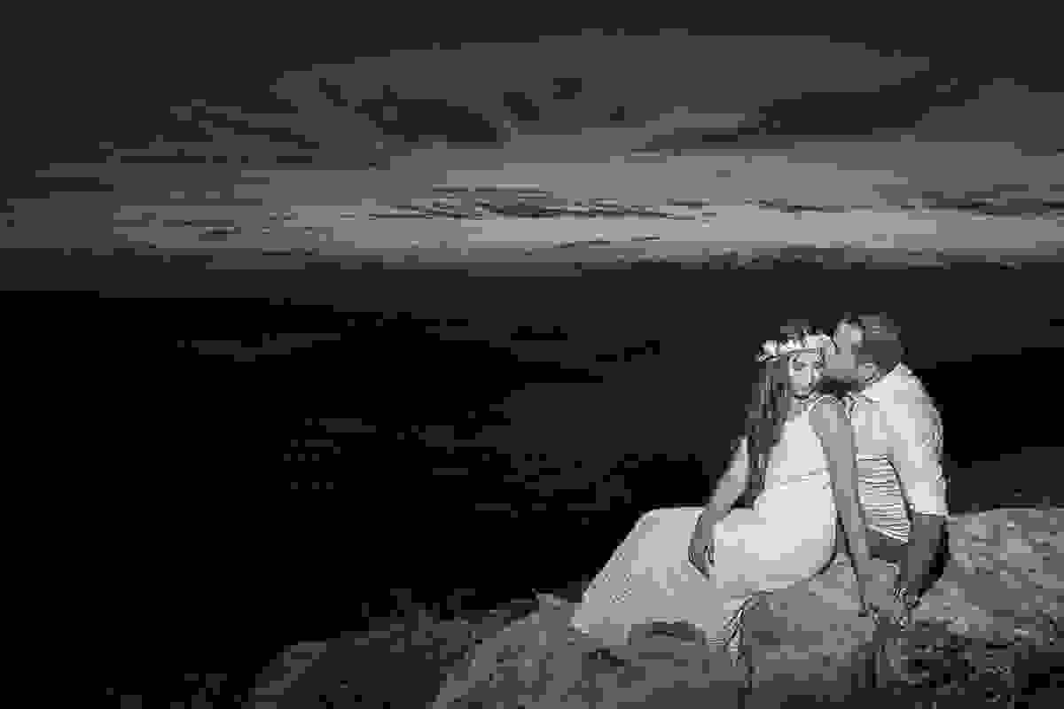 Fotografia de por do sol em arraial do cabo mostra casal sentado em uma pedra namorando diante do lindo espetáculo do por do sol