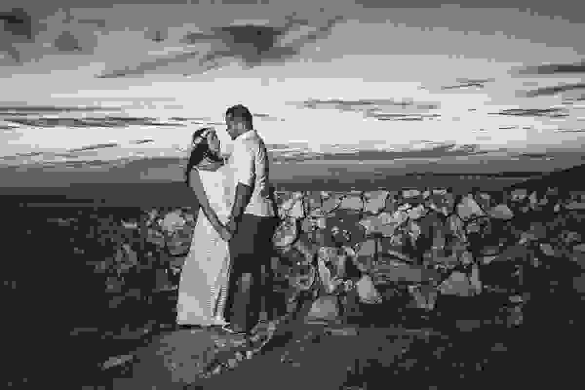 Ensao pré casamento em arraial do cabo mostra casal de pé encostado em uma mureta no alto do atalia de mãos dados se olhando um para o outro