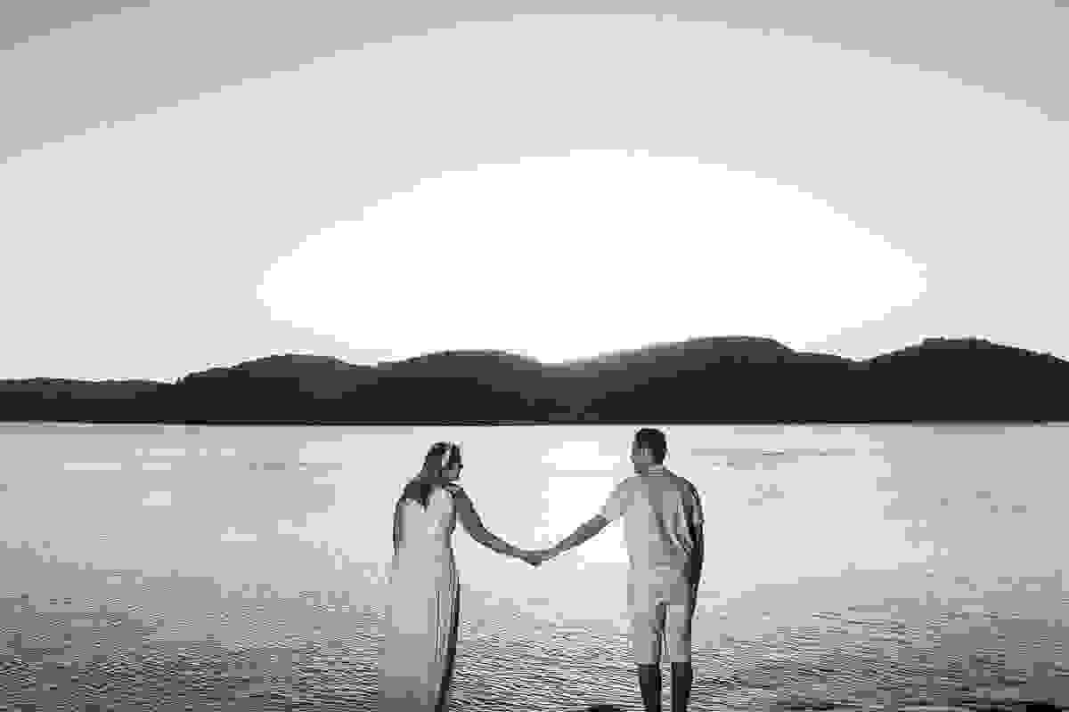 casal de mãos dadas de frente para o mar no nascer do sol por detrás das montanhas