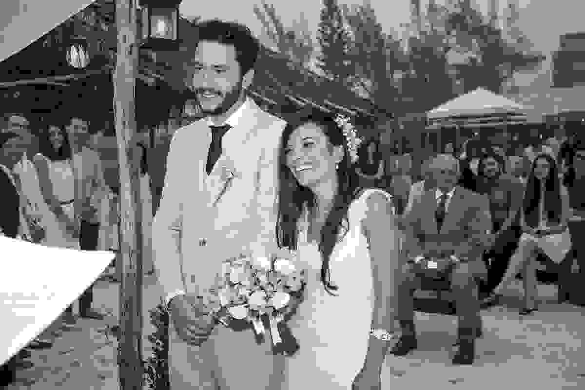 Noivo e noiva sorrindo para o celebrante enquanto acompanham a cerimonia do casamento