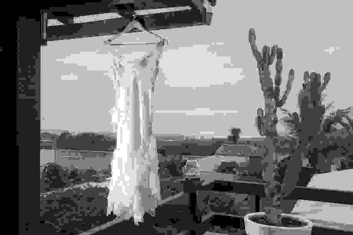 fotografo do casamento faz a foto do vestido da noiva pendurado em uma sacada com o mar de saquarema ao fundo