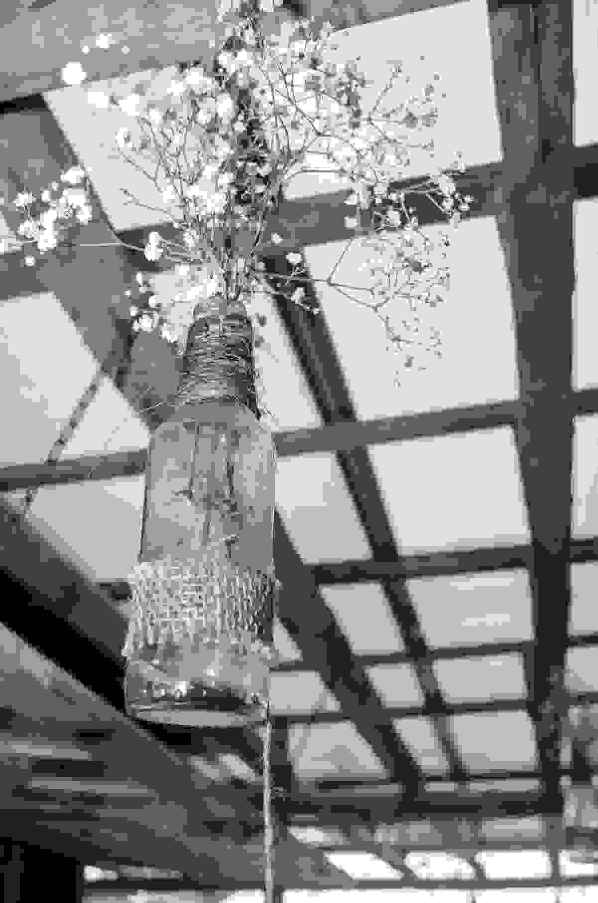 Garrafa pendurada com arranjo de flores do campo decorando o local da reepção do casamento