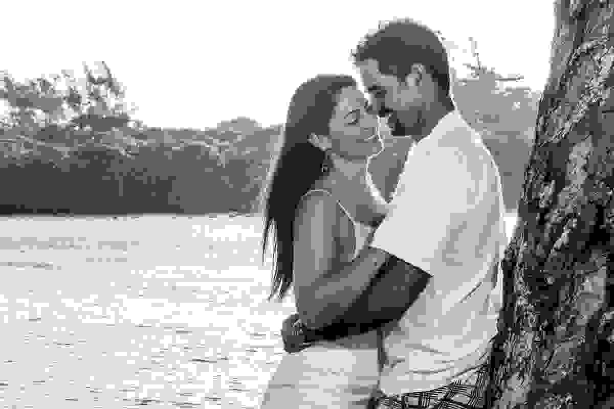 Casal abraçado em sessão pré wedding sorrindo e ao fundo o rio são joão
