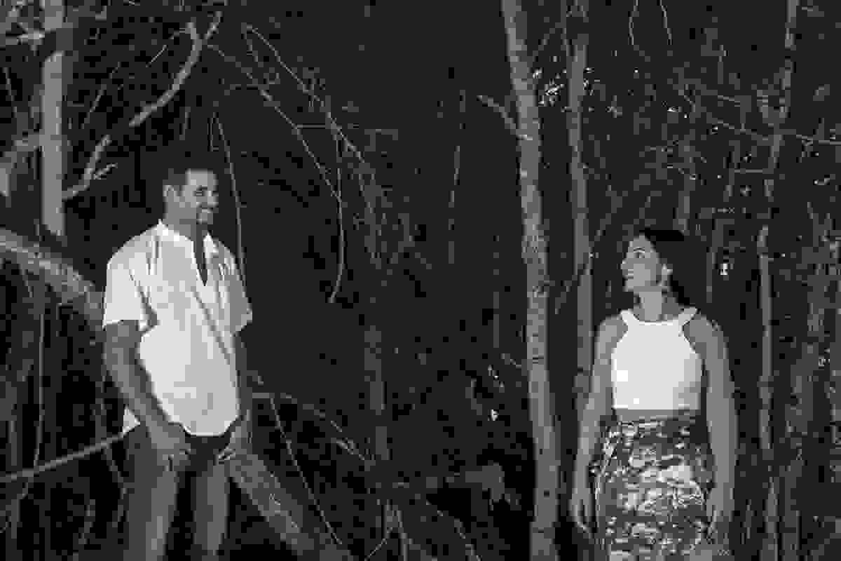 Ao fundo a vejetação do mangue e casal esta olhando um para o outro a uma certa distancia com um belo sorriso