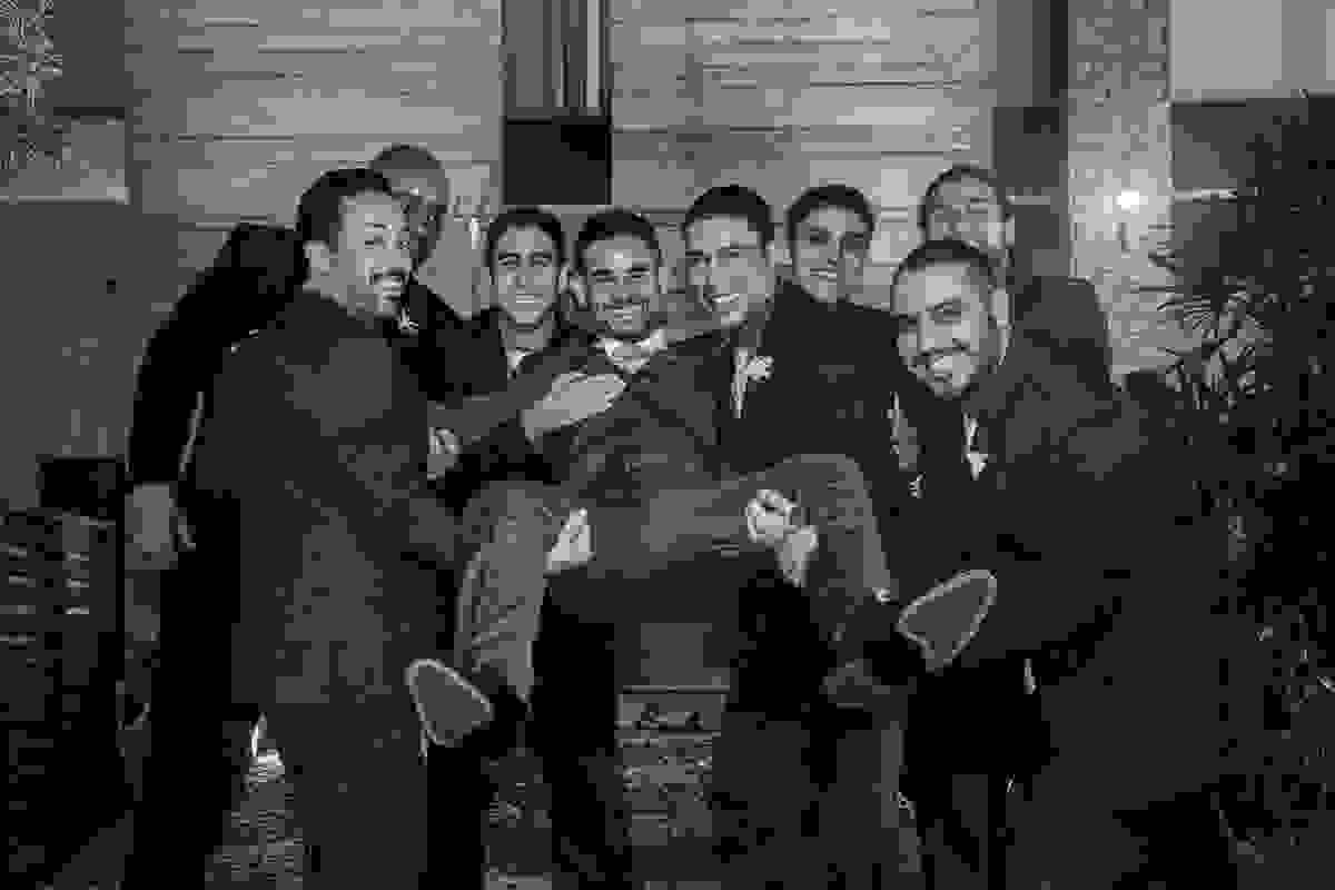 Padrinhos seguram noivo no colo em fotografia divertida do casamento