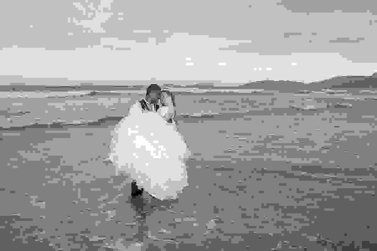 fotografia mostra noivos em cena carinhosa ele com ela no colo em ensaio de pós casamento feito na praia de geribar em armação dos búzios rio de janeiro