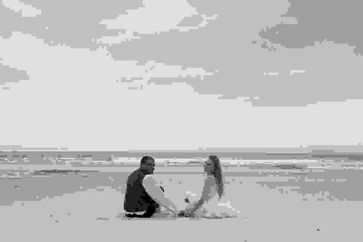 Noivos sentados na areia em fotografia Trahs The Dress de pós casamento em armação dos búzios