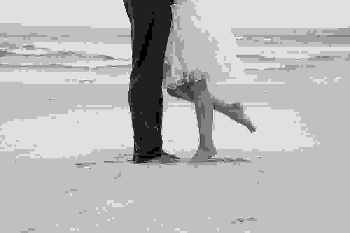 Fotografia em preto e branco do ensaio Trahs The Dress mostra os pés do casal e a noiva levantando um dos pés ensaio pós casamento