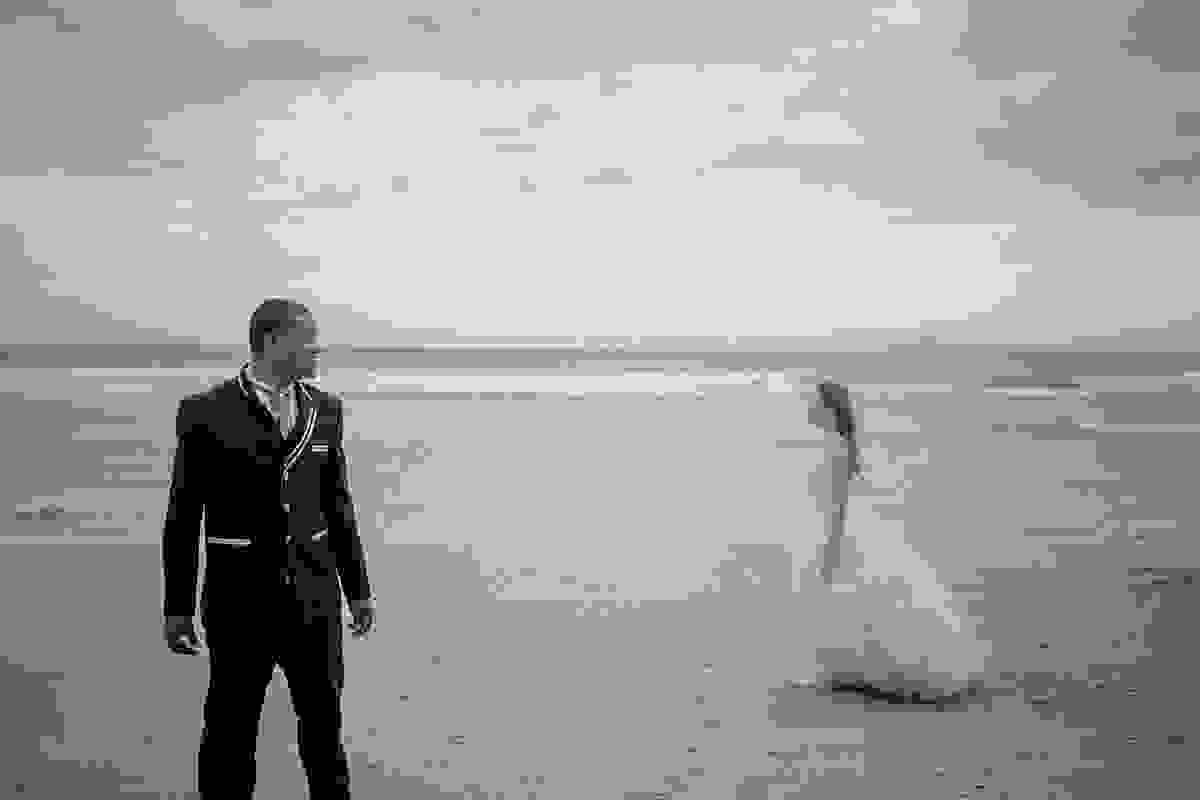 noivo em primeiro plano olhando noiva que atravesa a cena em foto artistica ensaio Trahs The Dress