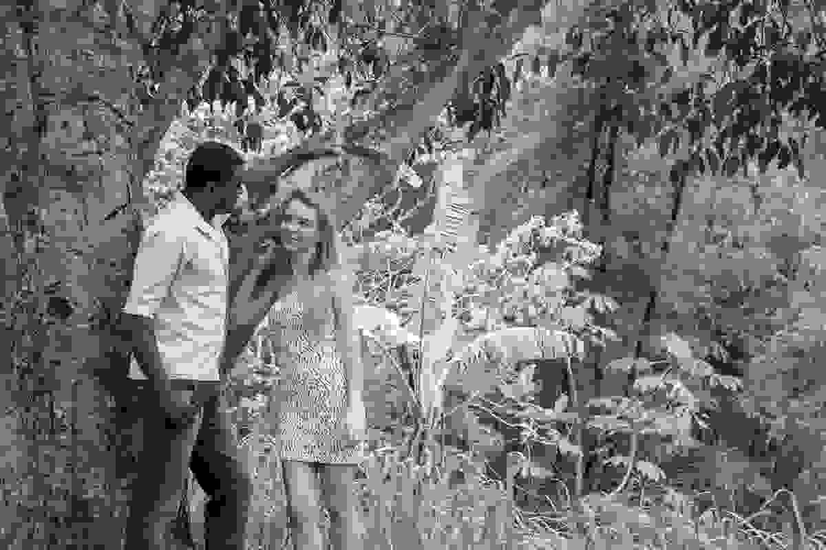 Noivo apoia a mão na arvore e faz charme para a noiva que sorri no ensaio pré casamento