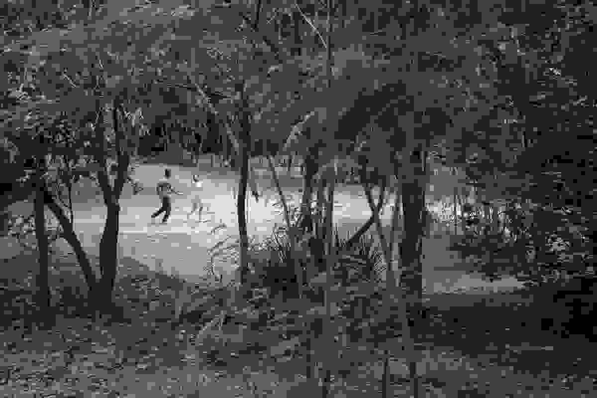 Casal corre de mãos dadas e foto é feita por entre as arvores que emolduram a cena ensaio de casamento