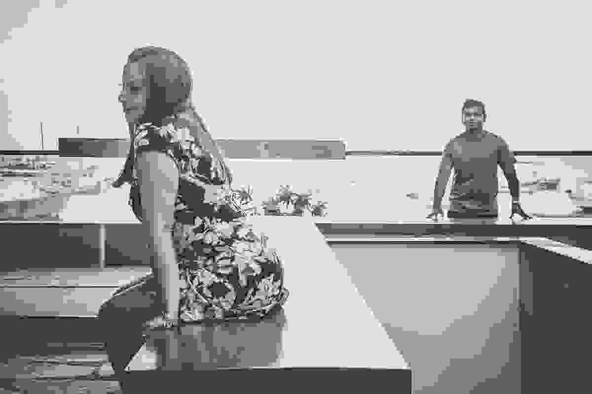 Ela esta sentada em uma mureta com um leve sorriso e ele olhando para ela de pé a distancia em fotografia preto e branco de ensaio pós casamento em Armação do Búzios Rio de Janeiro