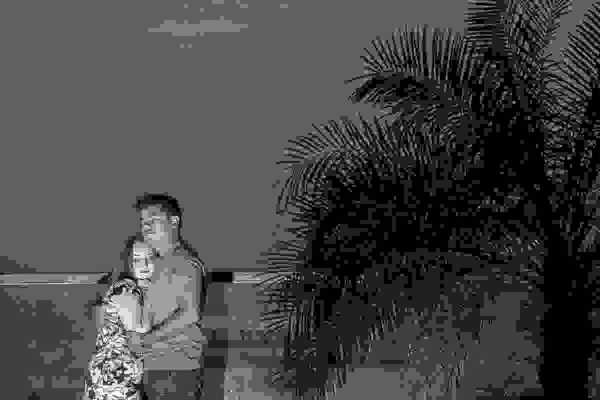 Casal abraçado a esquerda da imagem e a direita uma grande planta e ao fundo o mar da praia de armaçao dos Búzios no Rio de Janeiro