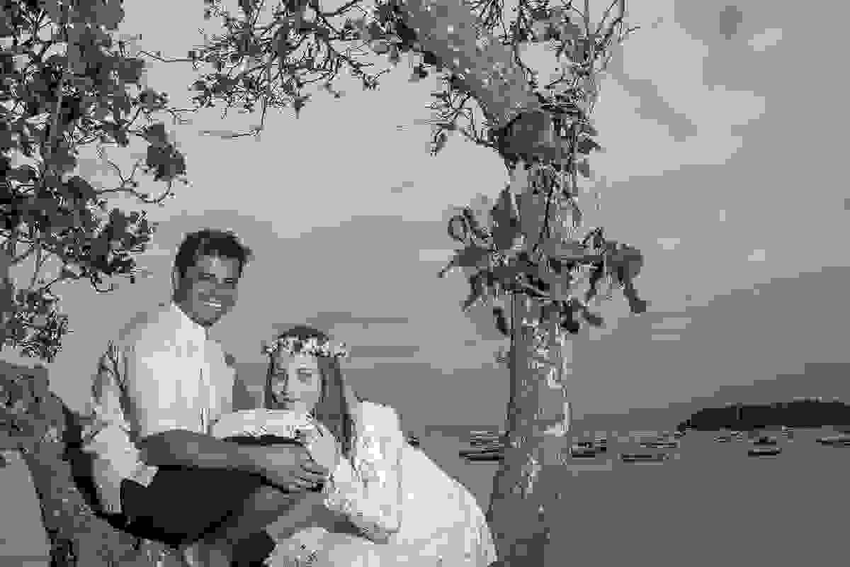 Casal sentado em uma arvore olhando para a camera em fotografia de ensaio pós casamento em armação dos búzios rio de janeiro