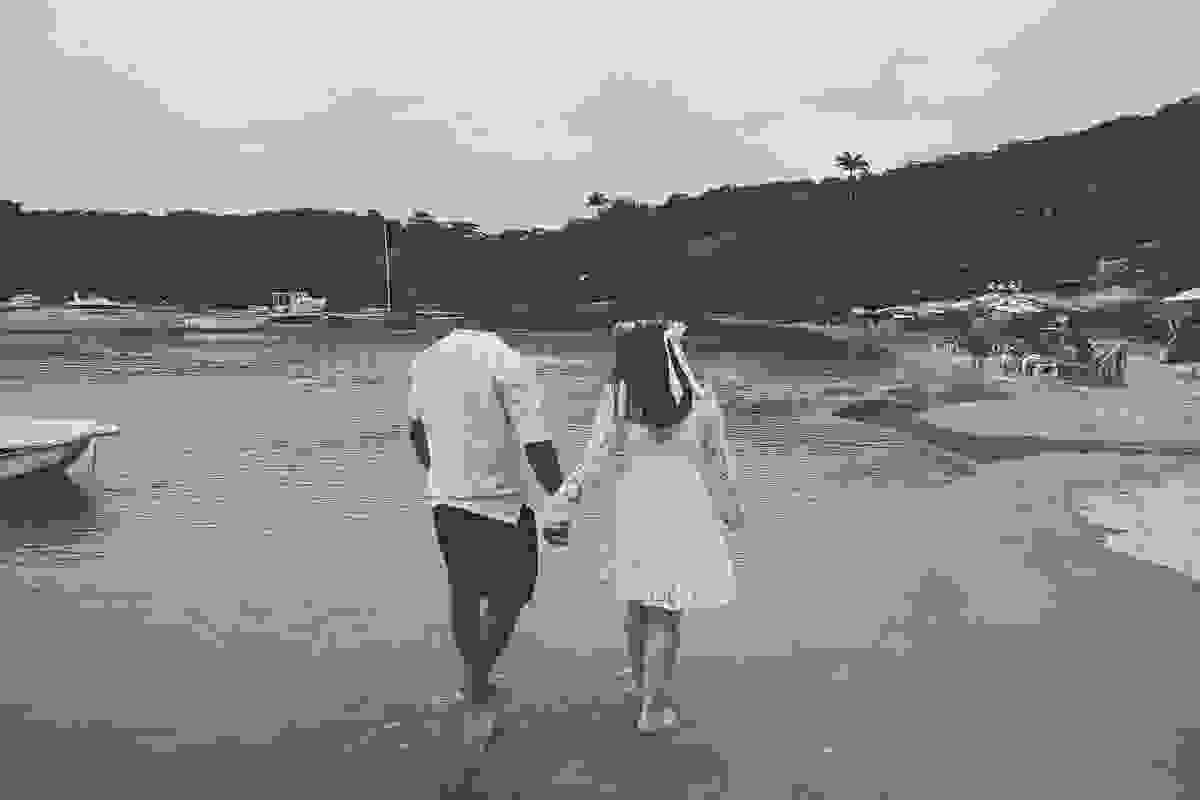 fotografia com tratamento envelhecido mostra casal caminhando pela praia dos ossos em armação dos búzios rio de janeiro em fotografia de pós casamento
