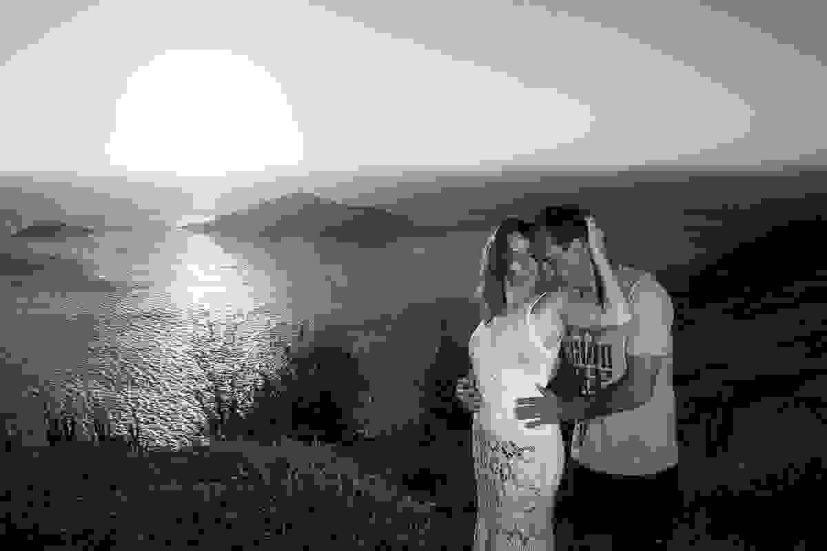 Fotografia romantica de casal no alto do atalaia e ao fundo um lindo por do sol
