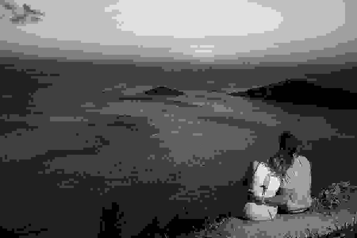 casal sentado e abraçados no alto do atalaia em arraial do cabo rio de janeiro olhando o por do sol