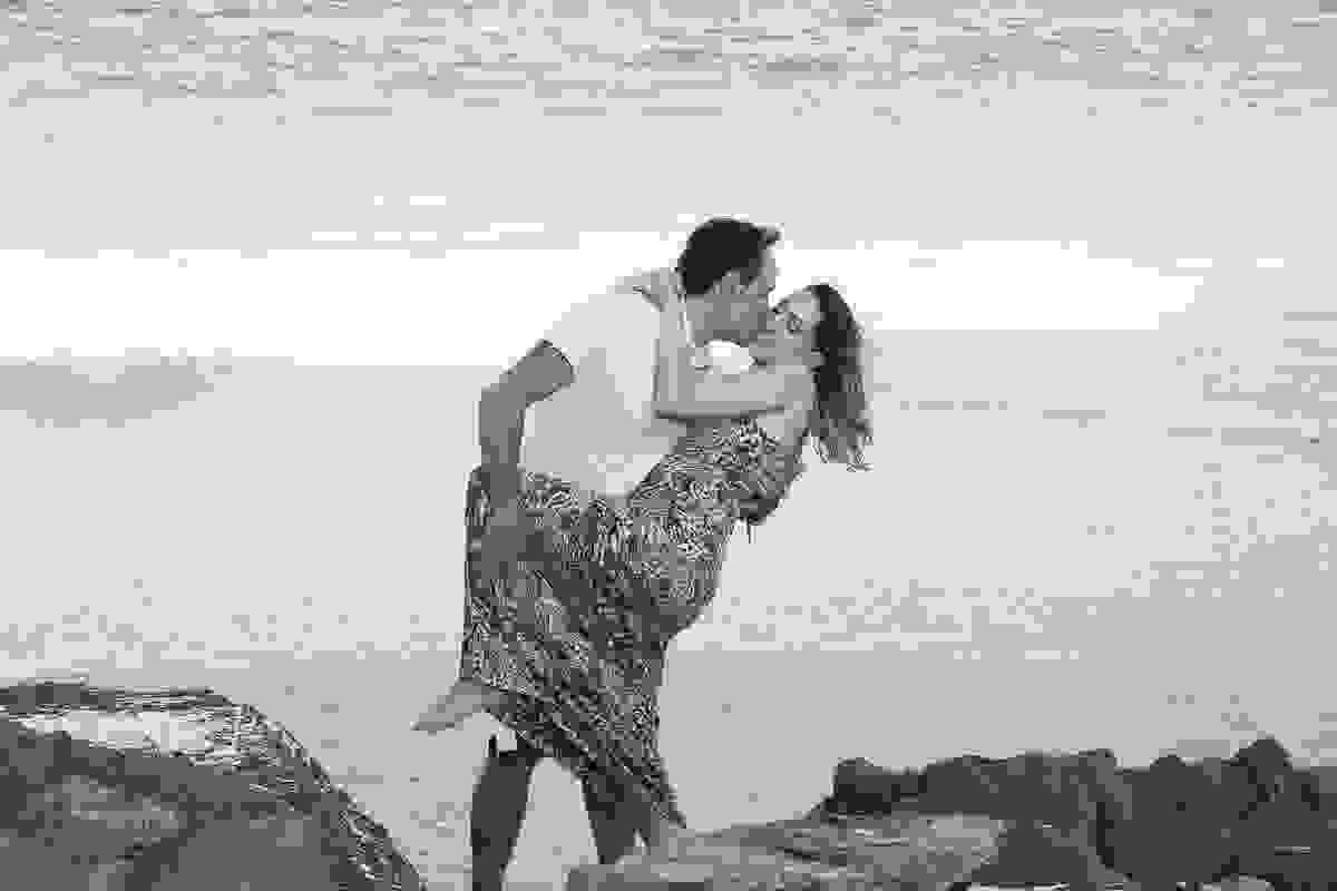 fotografia de casal mostra ele beijando o rosto dela enguanto a tomba para o lado em fotografia feita em arraial do cabo rio de janeiro pelo fotografo de casamento paulo ellias