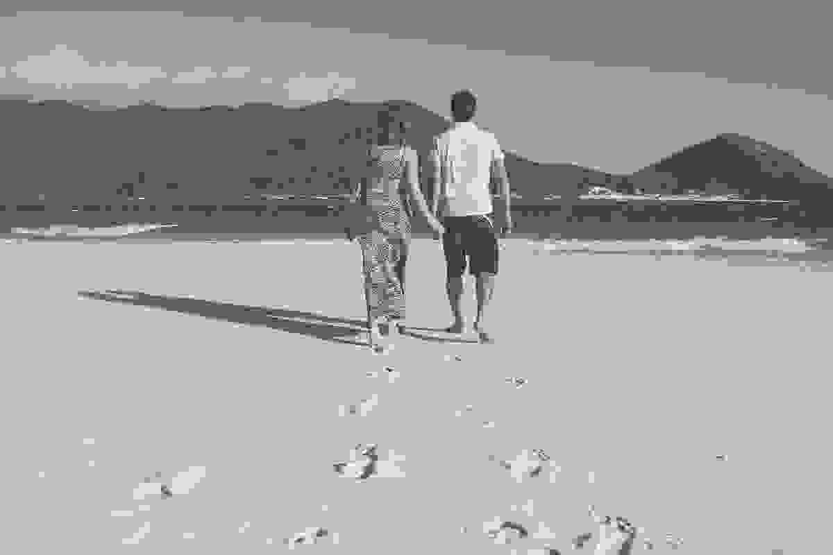 casal caminha na arreia da praia do atalaia em arraial do canbo rio de janeiro em fotografia feita pelo fotografo de casamento paulo ellias