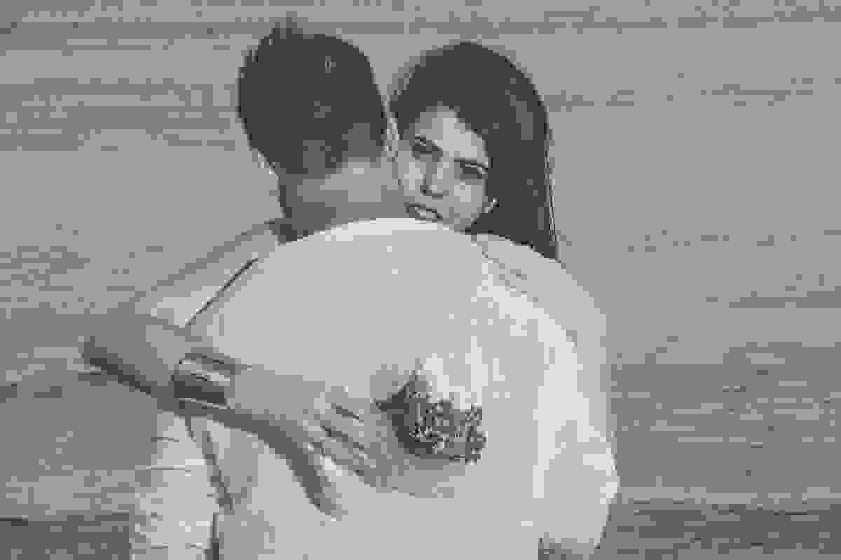 casal abraçado sendo que ele esta de costas e ela de frente com um bouquet de rosas na mão e atraz deles o mar da praia de geribar em búzios rio de janeiro