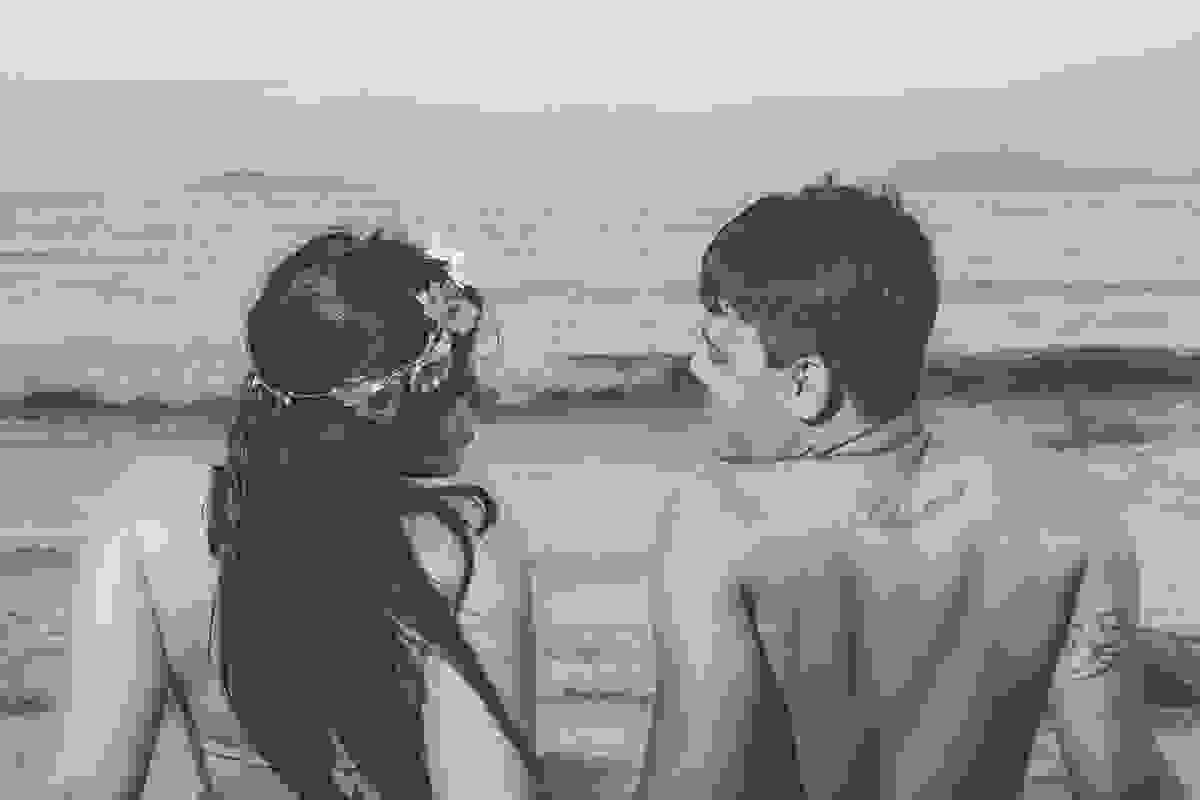 fotografia de ensaio pré casamento mostra casal de costas se olhando estado eles sentado de frente para a praia de geribar em búzios rio de janeiro