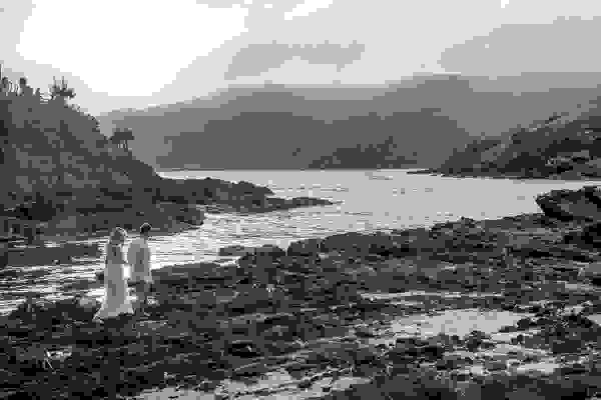 Fotografia de ensaio pré casamento que mostra o casal caminhando por entre as pedras na praia do forte são matheus em cabo frio rio de janeiro
