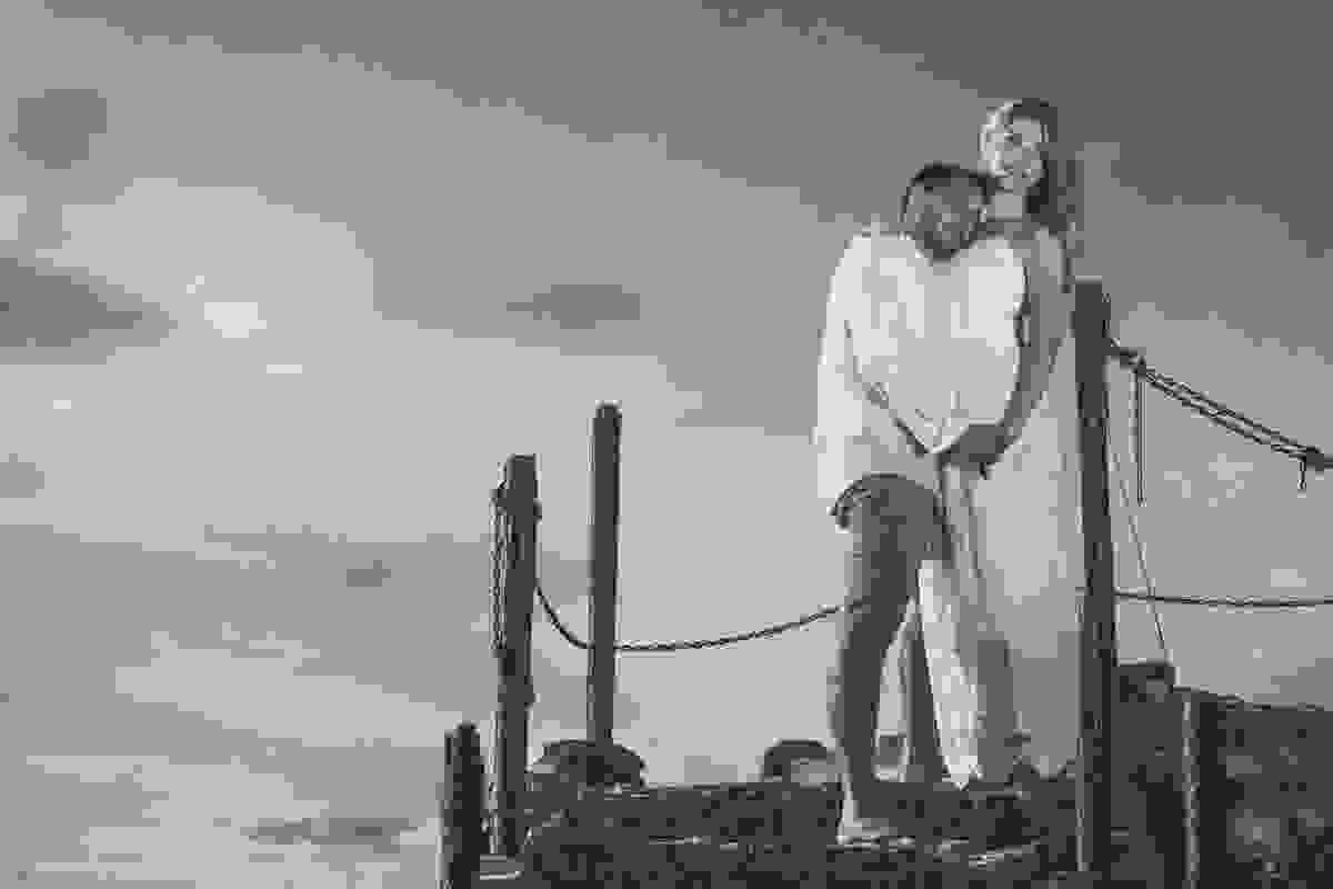 Casal em pé na escada que dá acesso ao forte são matheus em cabo frio rio de janeiro ele com a cabeça encontada no ombro dela em bela cena romantica