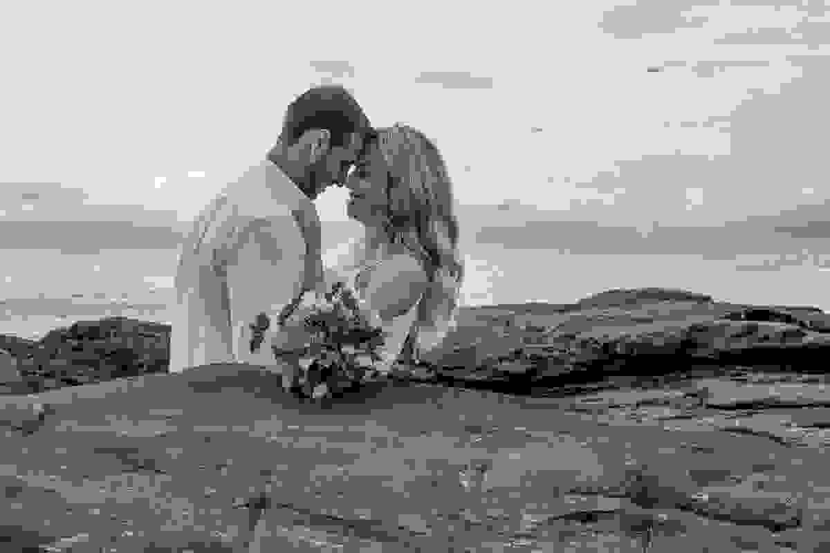 Lindo sorriso do casal por entre a pedras e o bouquet de noiva na frente nesta fotorgafia em cabo frio