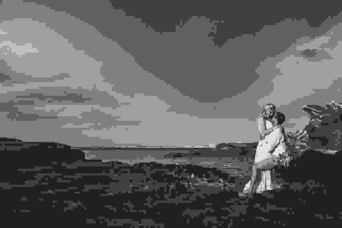 fotografia de pré casamento em cabo frio mostra o casal ele sentado em uma pedra e ele abraçada debriçada sobre ele