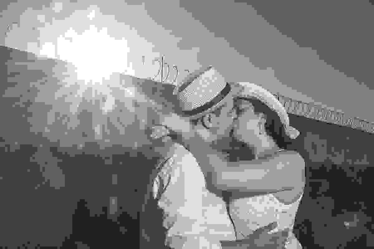 casal de noivos em fotografia pré casamento em arraial do cabo rio de janeiro se beijando, ela de braços entrelaçados em volta do pescoço dele e lindo raio de sol no canto da foto