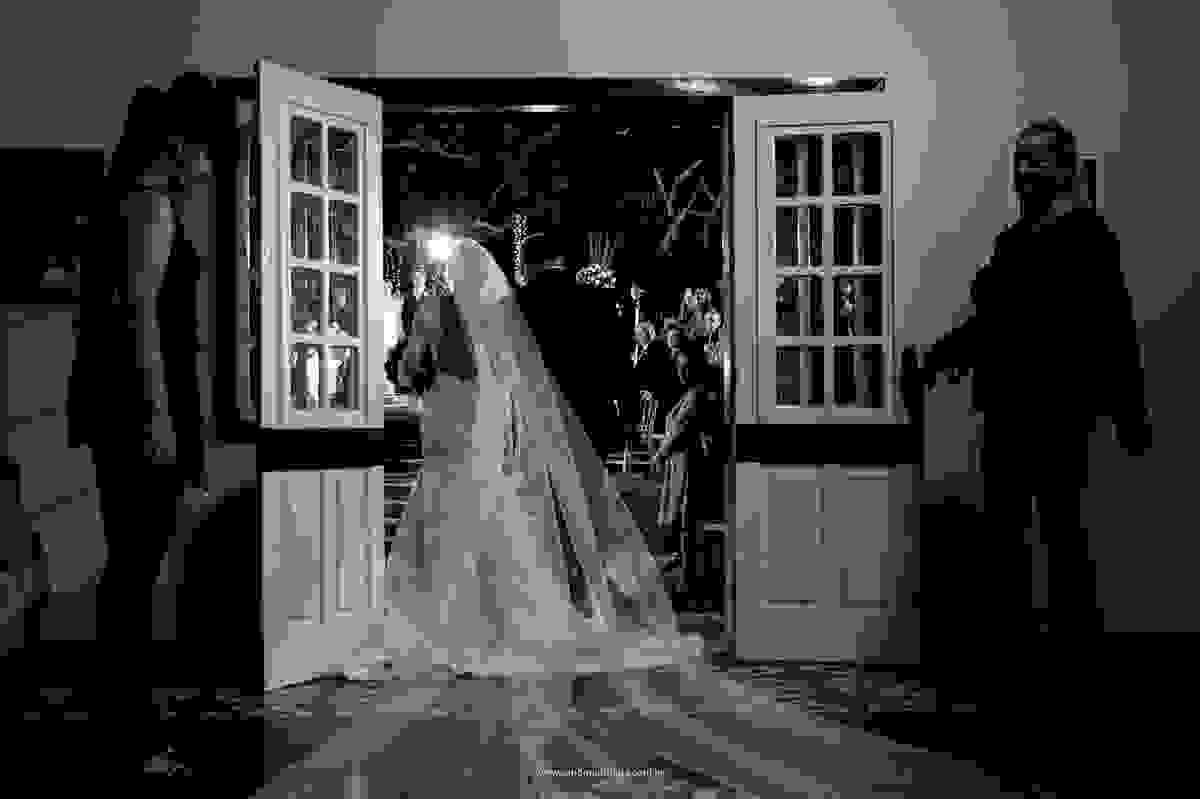 Momento imperdivel, feito pelo fotografo Sandro Andrade na entrada da noiva com seu pai e o noivo ao fundo vendo sua noiva linda, em um belíssimo vestido de noiva.