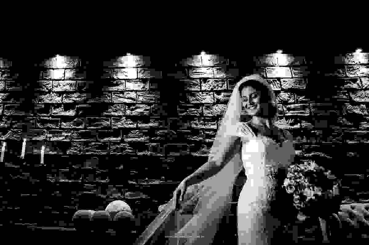 Um sorriso encantador, seu véu, o vestido e o buque magnifico, com uma bela iluminação em um preto e branco exuberante.