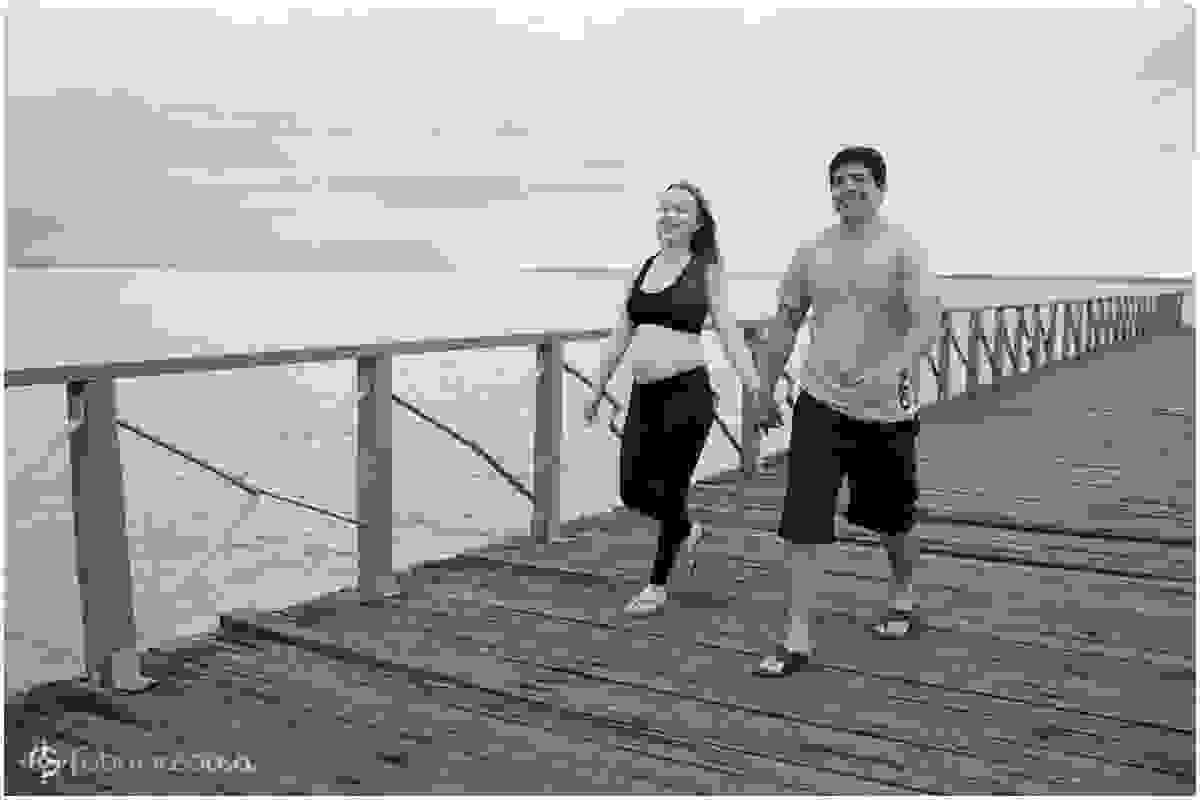 Mulher e homem grávidos caminham em deck de madeira de mãos dadas