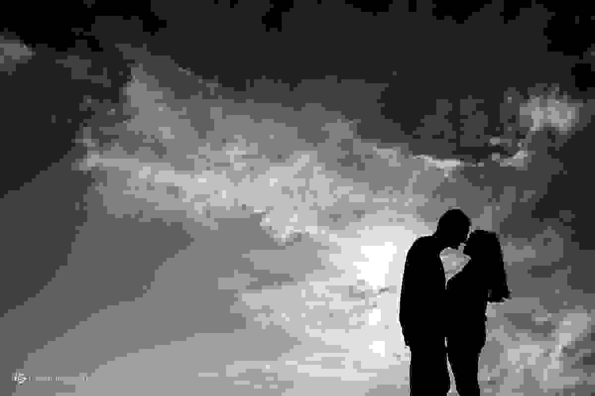 silhueta do casal quase se beijando com céu azul e muitas nuvens