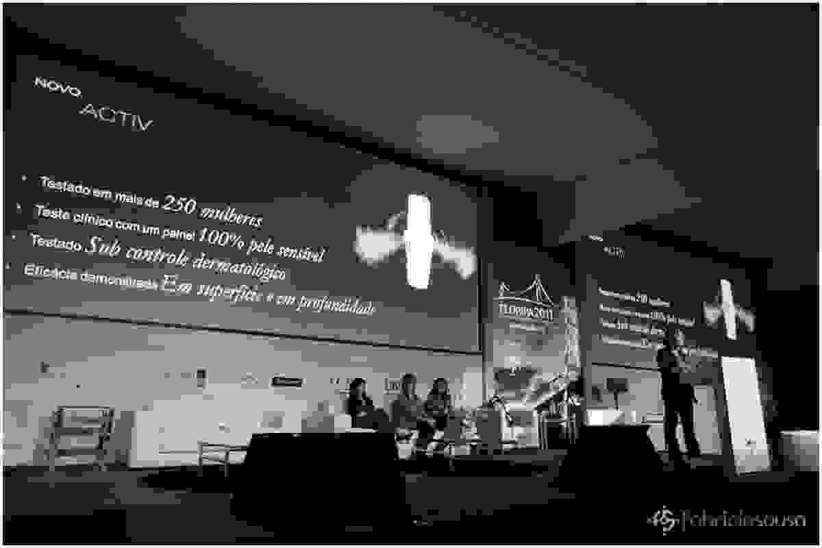 Geral do palco com telão projetado e palestrantes no palco