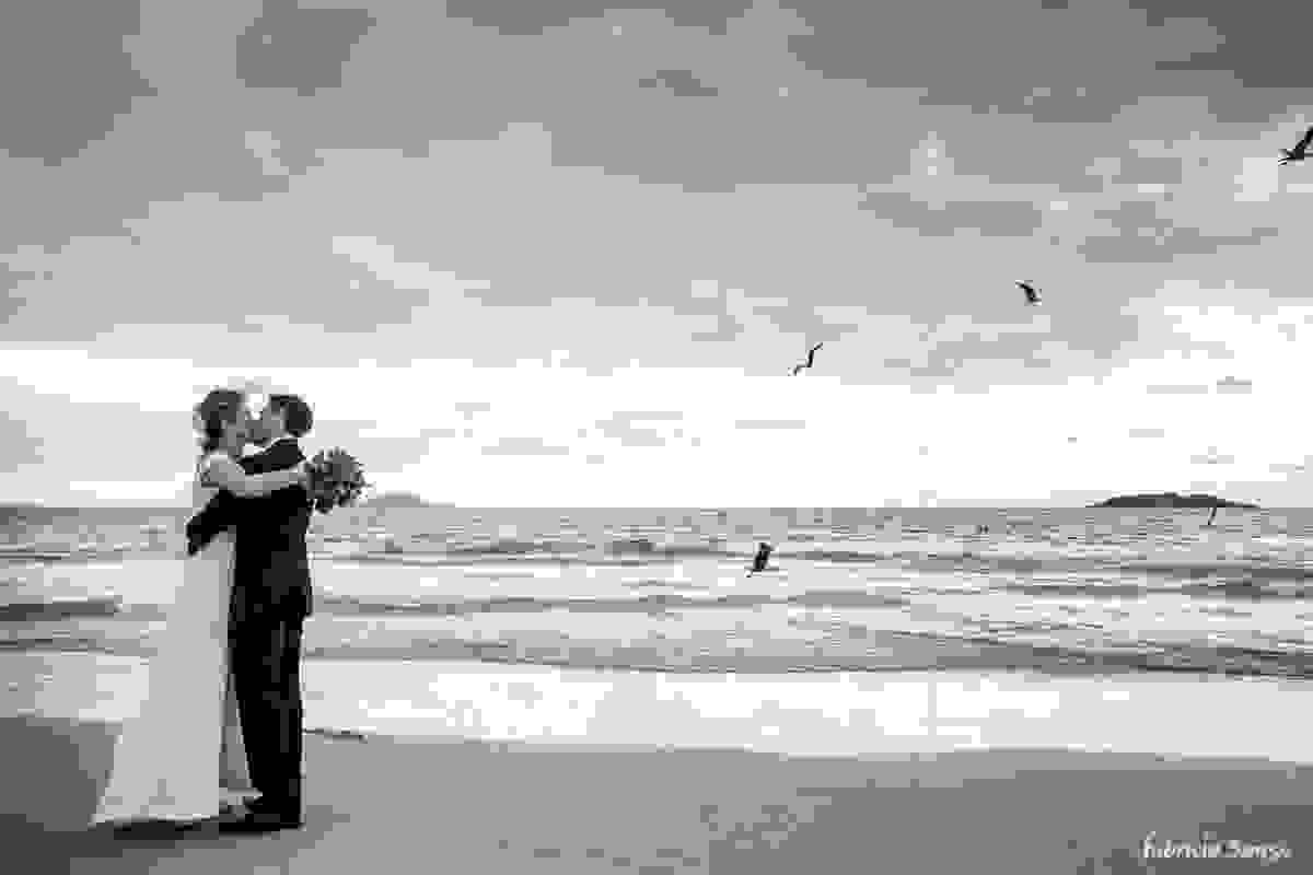 beijo do casal de noivos com gaivotes sobrevoando a praia