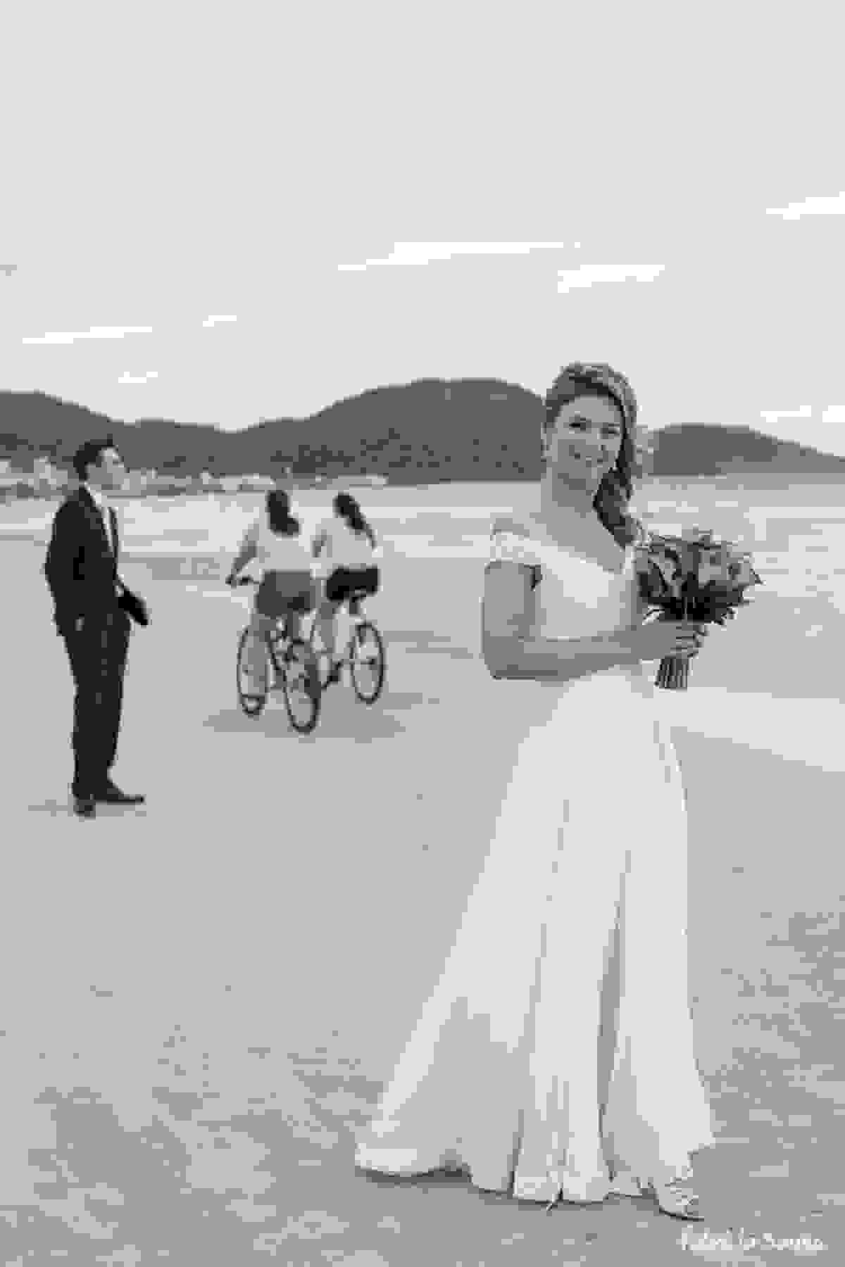 noiva com bouquet na praia - ciclistas passando na areia