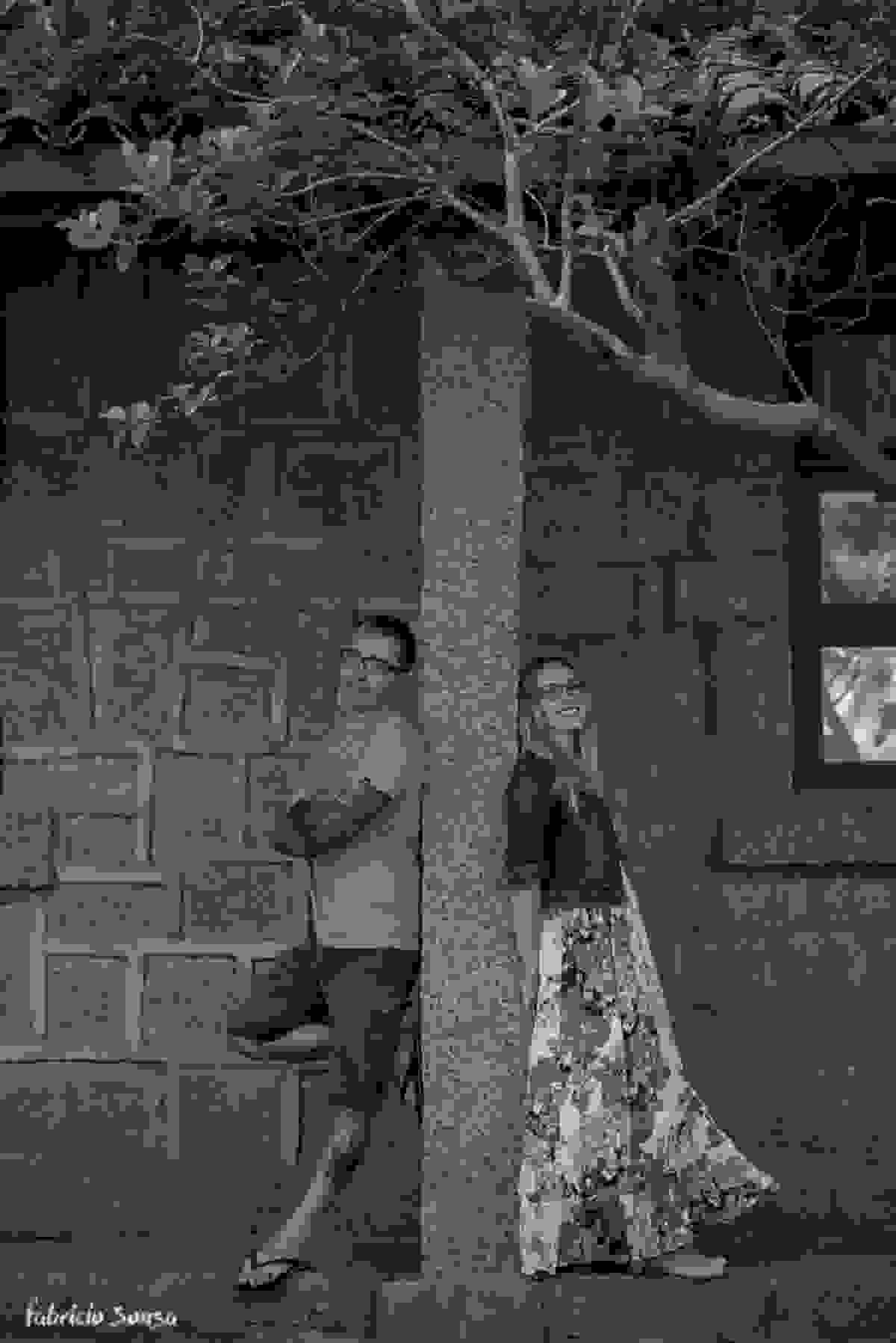 casal posa com muro de pedra e árvore singela no final do ensaio